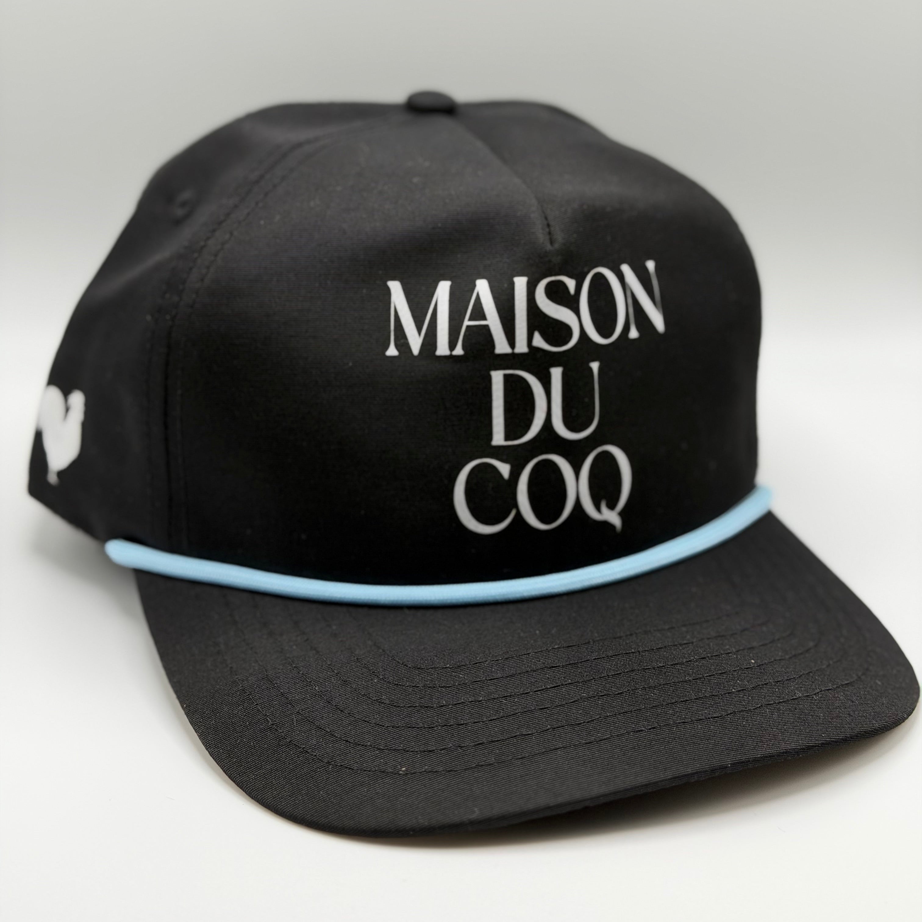 A black hat with blue rope and the text 'maison du coq' on the front with a rooster logo on the side