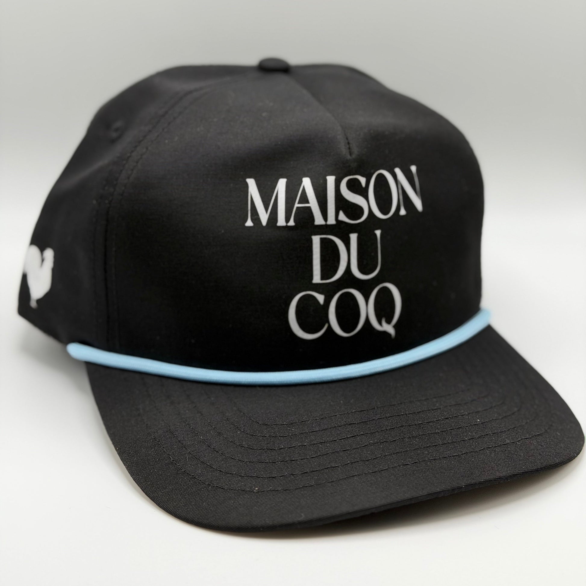 A black hat with blue rope and the text 'maison du coq' on the front with a rooster logo on the side